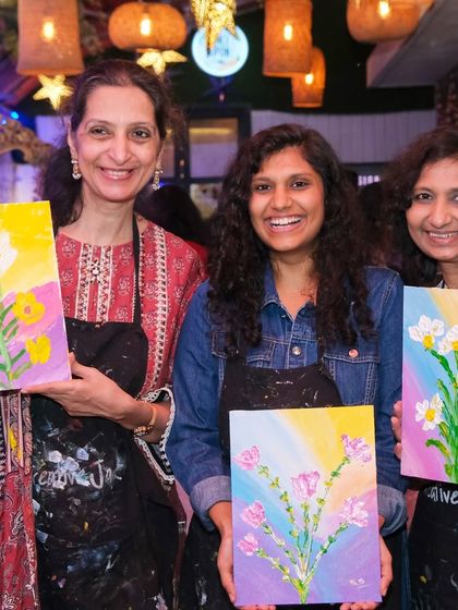 Three women smile as they display their beautiful floral paintings. The joy of creating something with your own hands is a universal feeling.