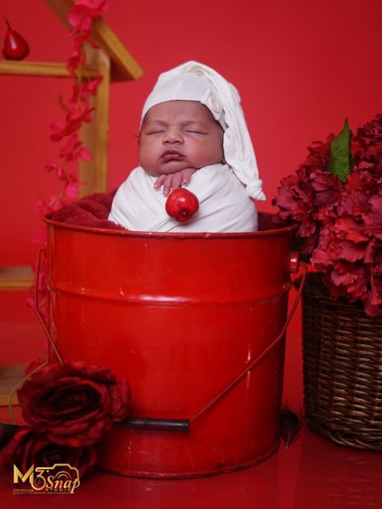 A newborn wrapped in white, resting in a bright red bucket. The contrast is so cheerful and fun, perfect for a vibrant portrait.