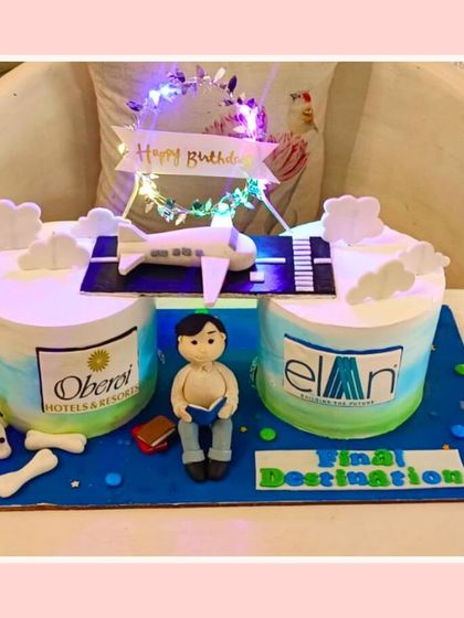 A farewell or corporate-themed cake featuring an airplane and logos from Oberoi and Elan.