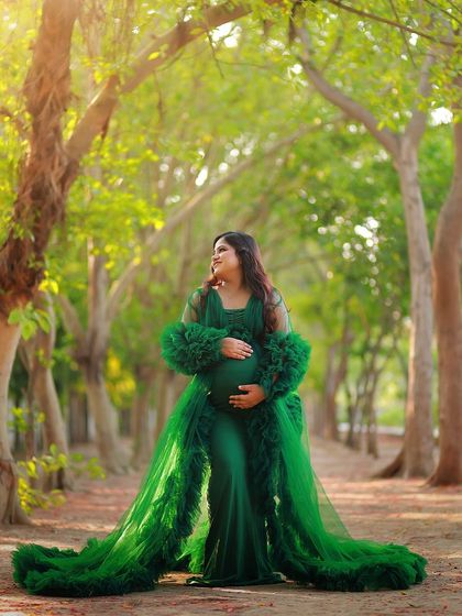 A full-length shot of the mother-to-be in a magnificent green gown, standing in a tree-lined path. This creates a sense of grandeur and enchantment.