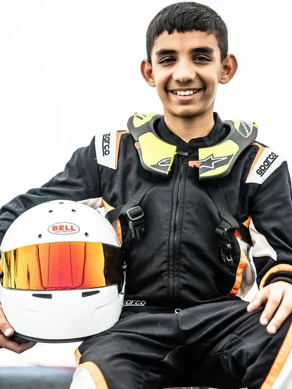 A junior driver smiles for the camera, holding his helmet.
