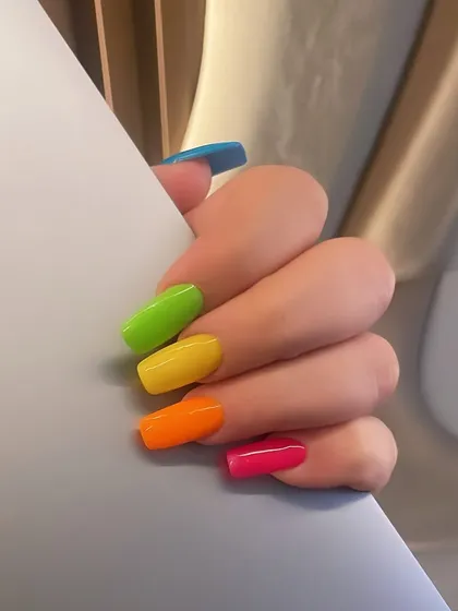 A vibrant, rainbow-colored set of nails. Each nail is painted a different bright, neon shade for a fun and playful look.