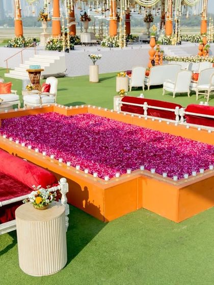 A unique seating element featuring traditional red velvet daybeds arranged around a custom structure filled with vibrant purple flowers.