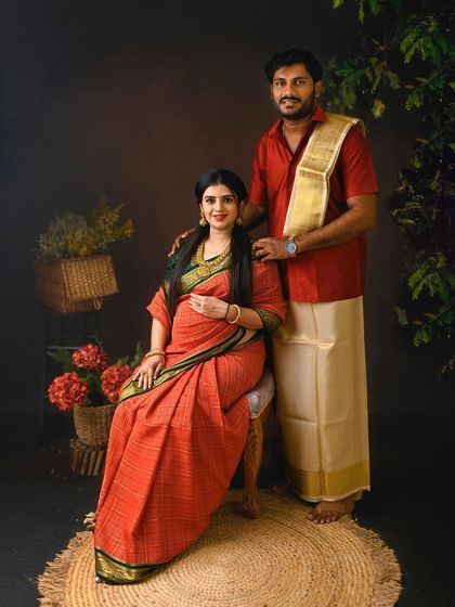 A classic South Indian couple's portrait. The traditional veshti and saree, combined with the rustic studio props, create a timeless and authentic image.