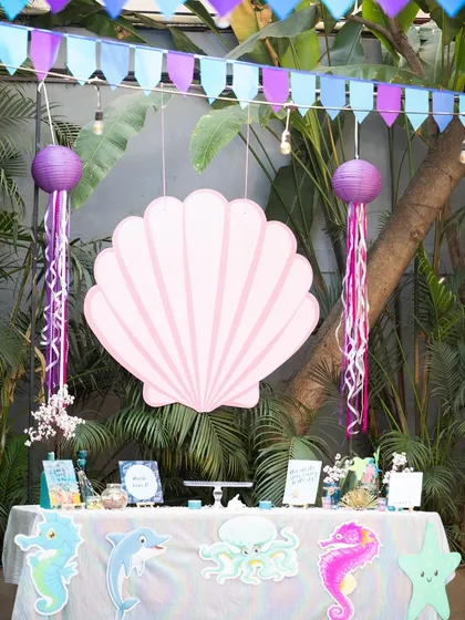 I transform your space into a different world. This under-the-sea themed party setup features a beautiful dessert table with a giant seashell backdrop, hanging jellyfish lanterns, and ocean-themed cutouts to create an immersive experience.