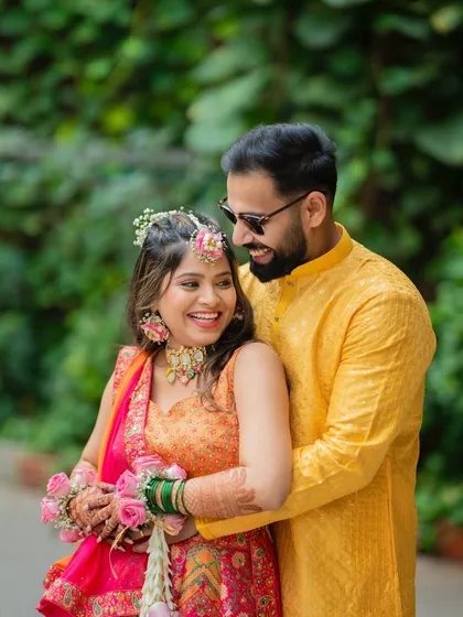 A happy couple portrait from their Haldi ceremony, showcasing the bride's beautiful floral jewelry and their coordinated yellow outfits.