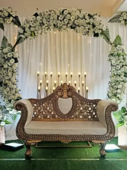 A full stage view of a half-saree ceremony at Thanisandra. The decor is clean and elegant, with a white floral arch, white drapes, and a beautiful golden sofa.