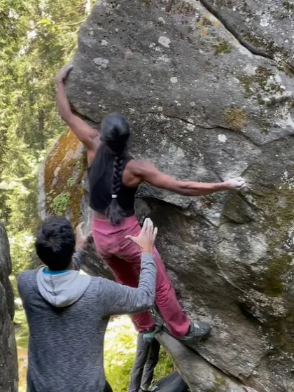 This photo captures the strength and balance required for bouldering, as a climber reaches for a hold with her spotter providing safety and confidence from below.