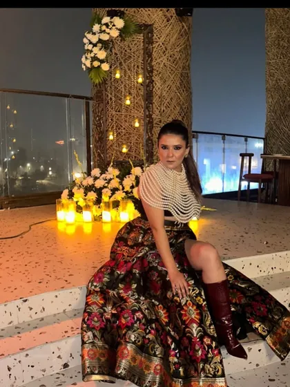 The founder, Pooja, sitting amidst a beautiful rooftop setup. The decor features natural textures, floral arrangements, and a warm glow from dozens of candles, showcasing our signature style.