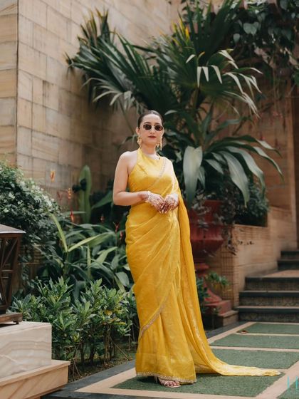 A full-length shot of the bride in her elegant yellow halter-neck saree, posing with confidence in a lush garden setting.