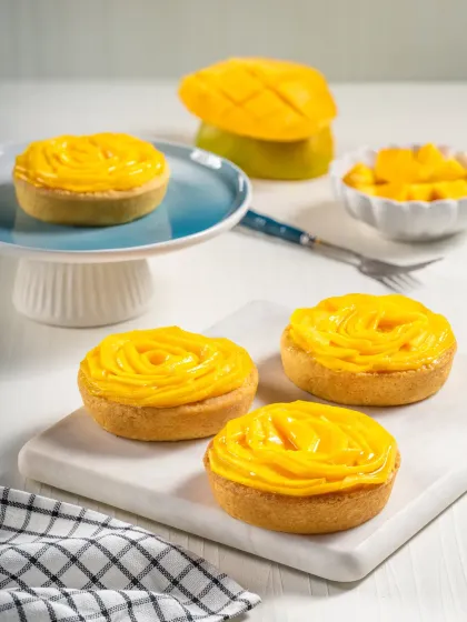 Individual mango tarts with beautifully arranged fruit on top, styled for a bakery's summer collection.