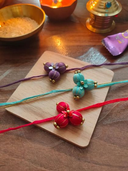 These beautiful floral rakhis are made from fabric beads and come in purple, teal, and red. Each one is carefully crafted by hand.