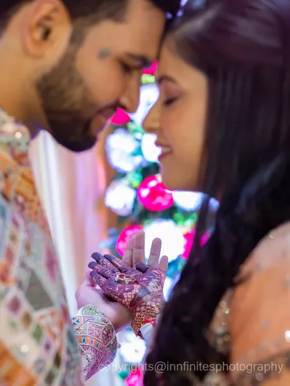 This shot beautifully combines the intimacy of the couple's pose with a detailed view of the bride's fresh mehendi, linking the pre-wedding rituals to the engagement celebration.