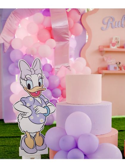 A life-sized Daisy Duck cutout stands next to a three-tiered pastel cake, adding a touch of classic Disney magic to the celebration.