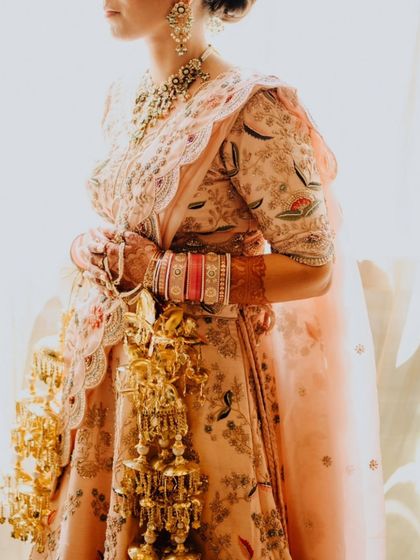 A detailed shot of the bride's pastel lehenga and her golden kaleeras, capturing the intricate beauty of her bridal attire.