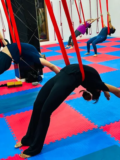 A group of students practices a supported backbend together, creating a wave of movement and energy across the studio floor.