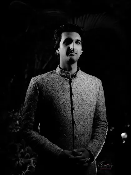 A powerful groom's portrait in black and white. The dramatic lighting creates a striking, classic look that emphasizes his sharp features and traditional attire.