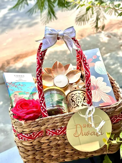 Bathed in natural light, this Diwali-themed jute basket is simply stunning. It's filled with premium chocolates, a lotus diya, a scented candle, and a decorative lantern, all brought together with a "Shubh Diwali" acrylic tag.