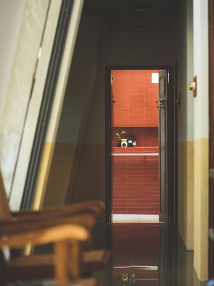 A glimpse from the living area into the bathroom, revealing the rich terracotta tile wall. This view highlights the deliberate framing of spaces and the consistent use of a warm, natural material palette throughout the home.