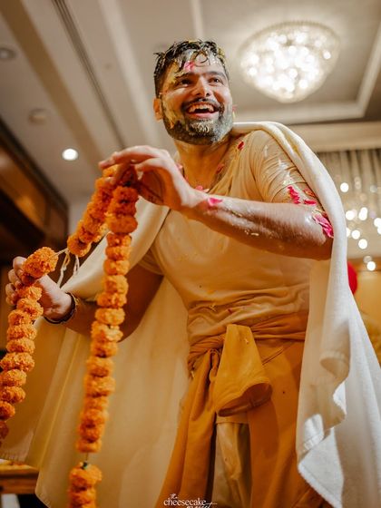 The groom, post-Haldi, playfully holding a marigold garland.