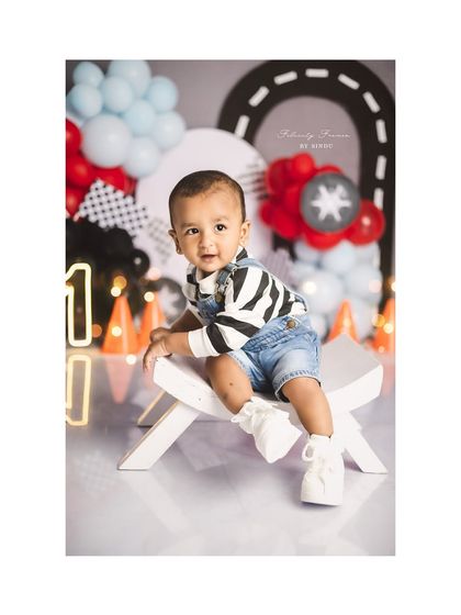 A cool little dude celebrating his first birthday. The race car theme with checkered flags and balloons sets a fun and energetic mood.