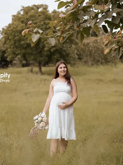 A beautiful solo shot of the mom-to-be walking through the field, holding a bouquet of white flowers. Her simple white dress and the natural setting create a pure and gentle portrait.