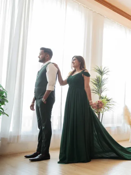 A quiet, reflective moment by the window. The bride's hand on the groom's shoulder and their shared gaze outwards create a feeling of partnership and shared dreams.