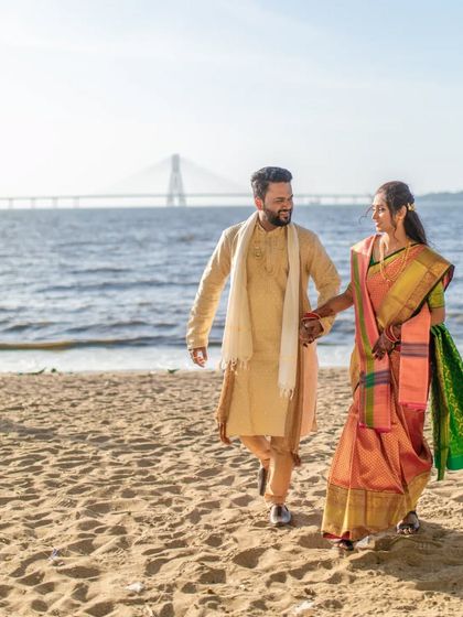 A beautiful shot of the couple walking on the beach with the Bandra-Worli Sea Link in the background, a classic Mumbai wedding portrait.