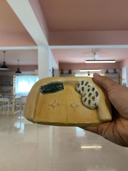 Holding up a finished piece from the "Paint-A-Pot" workshop. This miniature couch, complete with tiny pillows, is a testament to the fun and creativity that happens in our studio.