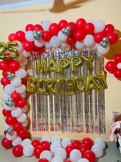 A classic red, white, and silver balloon arch for a 25th birthday. The setup includes a shimmer curtain and foil balloons for the name and age.