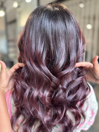 A stylist's hands frame the beautiful burgundy waves, showing off the volume and shine.