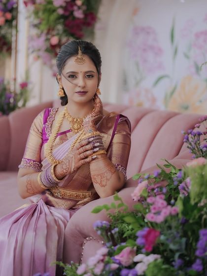 The bride-to-be looks radiant against the engagement decor. The soft lighting and the abundance of fresh flowers in shades of lavender and pink complement her beautiful silk saree perfectly.
