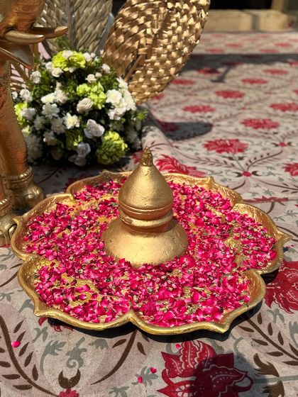 A traditional golden urli filled with water and vibrant pink rose petals, a classic decor piece that symbolizes prosperity and beauty in Indian culture.