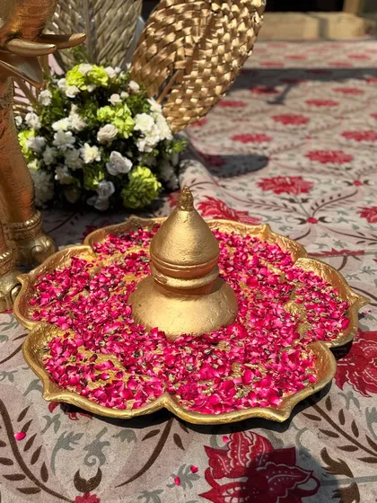 A traditional golden urli filled with water and vibrant pink rose petals, a classic decor piece that symbolizes prosperity and beauty in Indian culture.