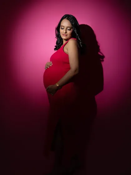For the mom-to-be who loves a touch of drama. I used a single spotlight against a bold pink backdrop to sculpt the light, highlighting her beautiful silhouette in this vibrant red dress for a powerful and glamorous maternity portrait.