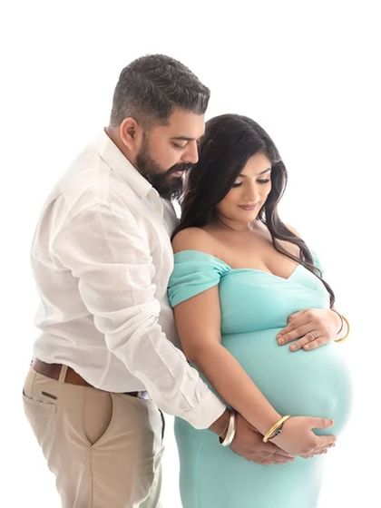 An intimate couple's shot where both partners gently hold the baby bump. The coordinated white and blue outfits complement the bright and airy feel of the studio session.