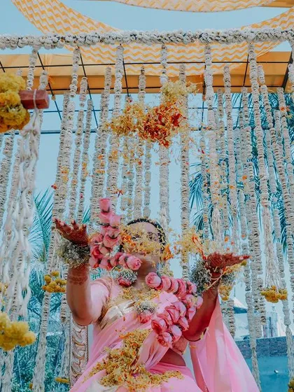 A traditional 'phoolon ki holi' or flower shower for the bride during her Haldi ceremony. The setup includes beautiful hangings of marigolds and tuberoses.