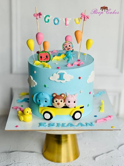 A delightful Cocomelon cake for Eeshaan's first birthday. This design features JJ and his animal friends in a yellow car, surrounded by clouds and colorful decorations.