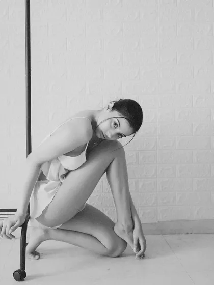 A simple, minimalist black and white shot. The model's pose is fluid and graceful, using a clothing rack as a prop to create interesting lines and shapes.