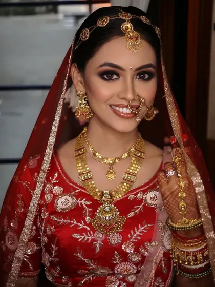 A full bridal portrait showcasing the elegant red lehenga, intricate gold jewelry, and the timeless makeup look I created for her.