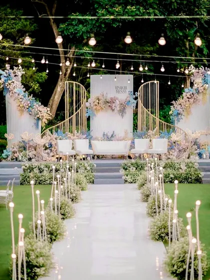A breathtaking outdoor wedding stage with pastel blue and pink florals. The curved, modern backdrop and illuminated aisle create a dreamy, fairytale setting.