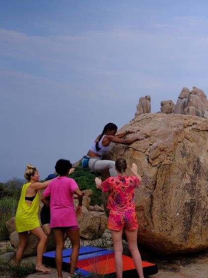 A group of women spotting a climber while ensuring the crash pads are perfectly placed below. This combination of active spotting and proper pad placement is key to safe bouldering.