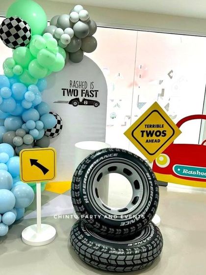 A "Two Fast" car-themed second birthday party. The decoration includes a balloon arch, road signs, a car cutout, and tire props for a fun racing vibe.