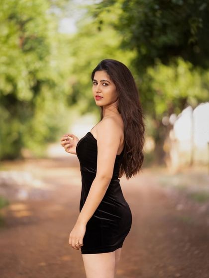 A simple yet striking black velvet mini dress shot outdoors. The contrast between the dress and the natural green background makes the subject pop.