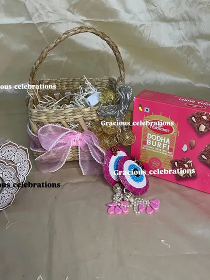 Celebrate Diwali with this festive basket filled with traditional treats. It includes a box of Dodha Burfi, decorative evil eye hangings, and fairy lights to add sparkle to the celebration.