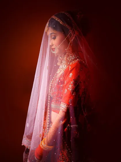 A moody side-profile portrait of a bride under a sheer veil, using shadows and red light to create a dramatic effect.