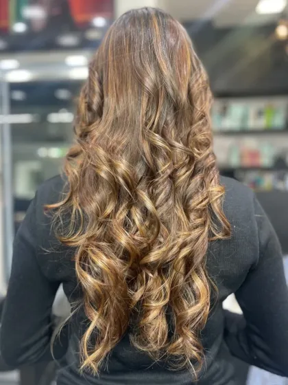 The back view of long hair styled in perfect, glamorous curls with beautiful caramel highlights.