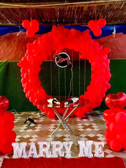 A clear, straight-on shot of the red-themed proposal decor. You can see the details like the heart-shaped foil balloons on top of the pillars and the delicate fairy lights around the "Love" sign.