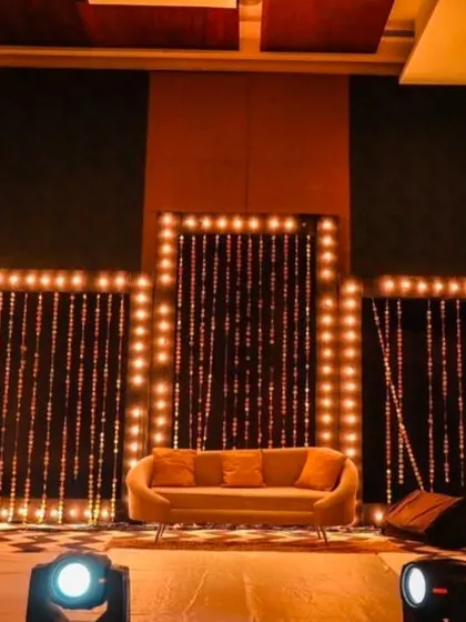 A minimalist yet impactful sangeet stage. The backdrop features simple panels with bulb lighting, creating a warm and inviting focal point for performances.