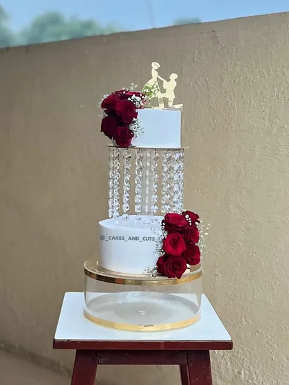 This stunning wedding cake uses crystal chandelier separators to create a floating effect. Adorned with fresh red roses and a proposal silhouette topper, it's a romantic and elegant choice for any wedding reception.